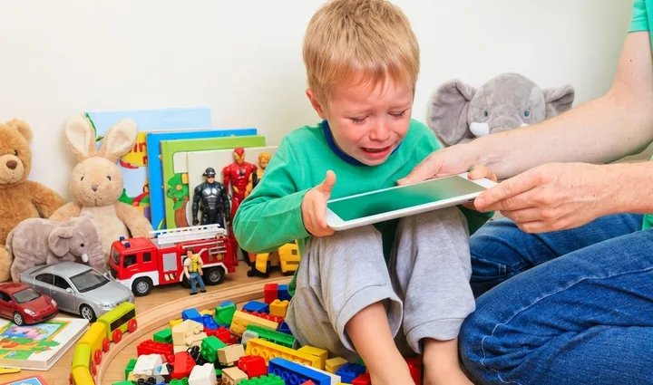 Niño llorando cuando le quitan la tablet, rodeado de juguetes